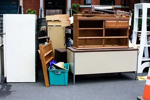 Furniture and household items stacked on a dolly beside a white refrigerator outdoors