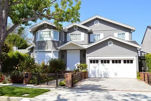 Two-story gray suburban house with white trim, front porch, garage, and landscaped yard.