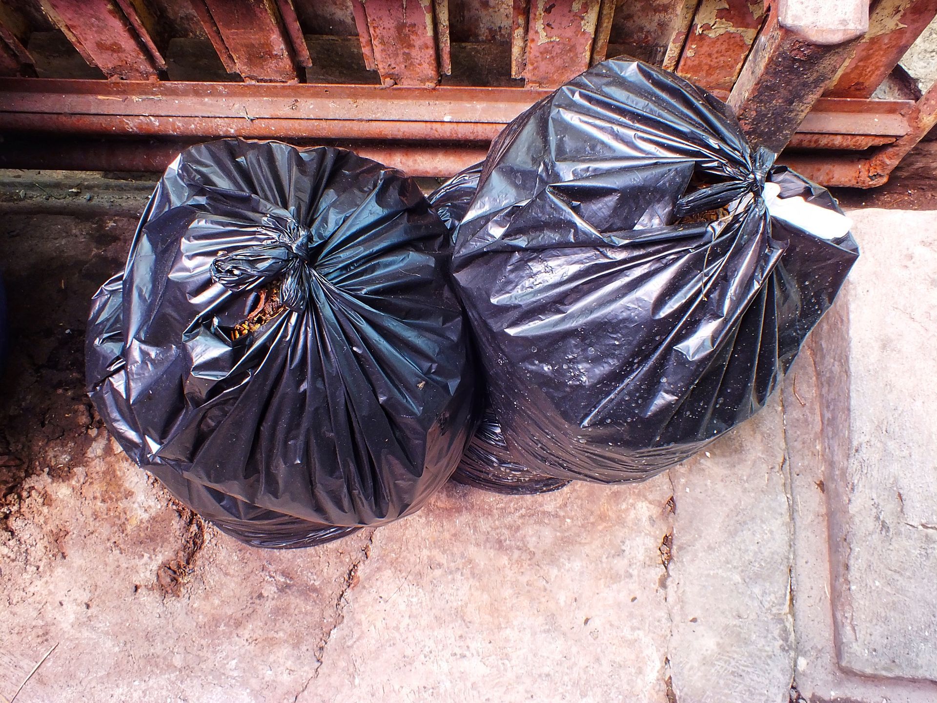 Two black garbage bags on a concrete floor beside a brick wall.