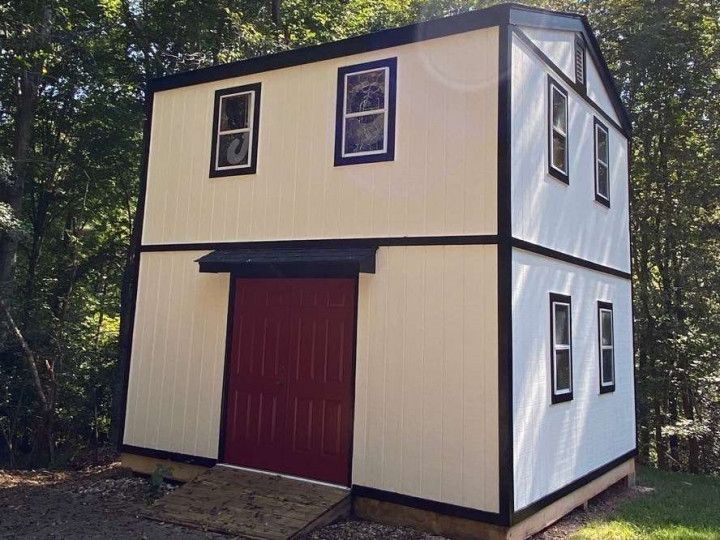 Two-story cream and white shed with black trim and a red barn door; windows with black frames.