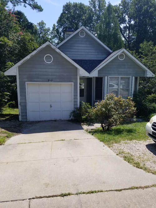 Gray house with a white garage door, small shrubs, and a concrete driveway.