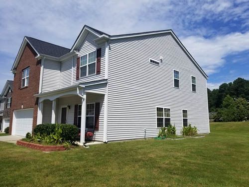 Townhouse exterior with light gray siding, dark shutters, and green lawn under a blue sky.