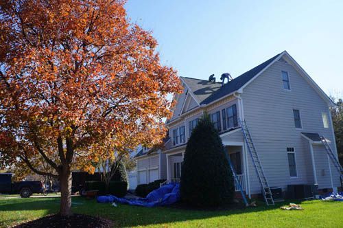 Two roofers on a house roof; fall foliage and blue tarp on the ground.