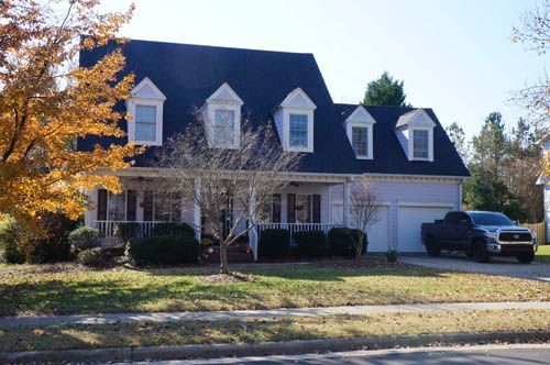 Two-story gray house with a black roof, white trim, and a truck parked in the driveway.