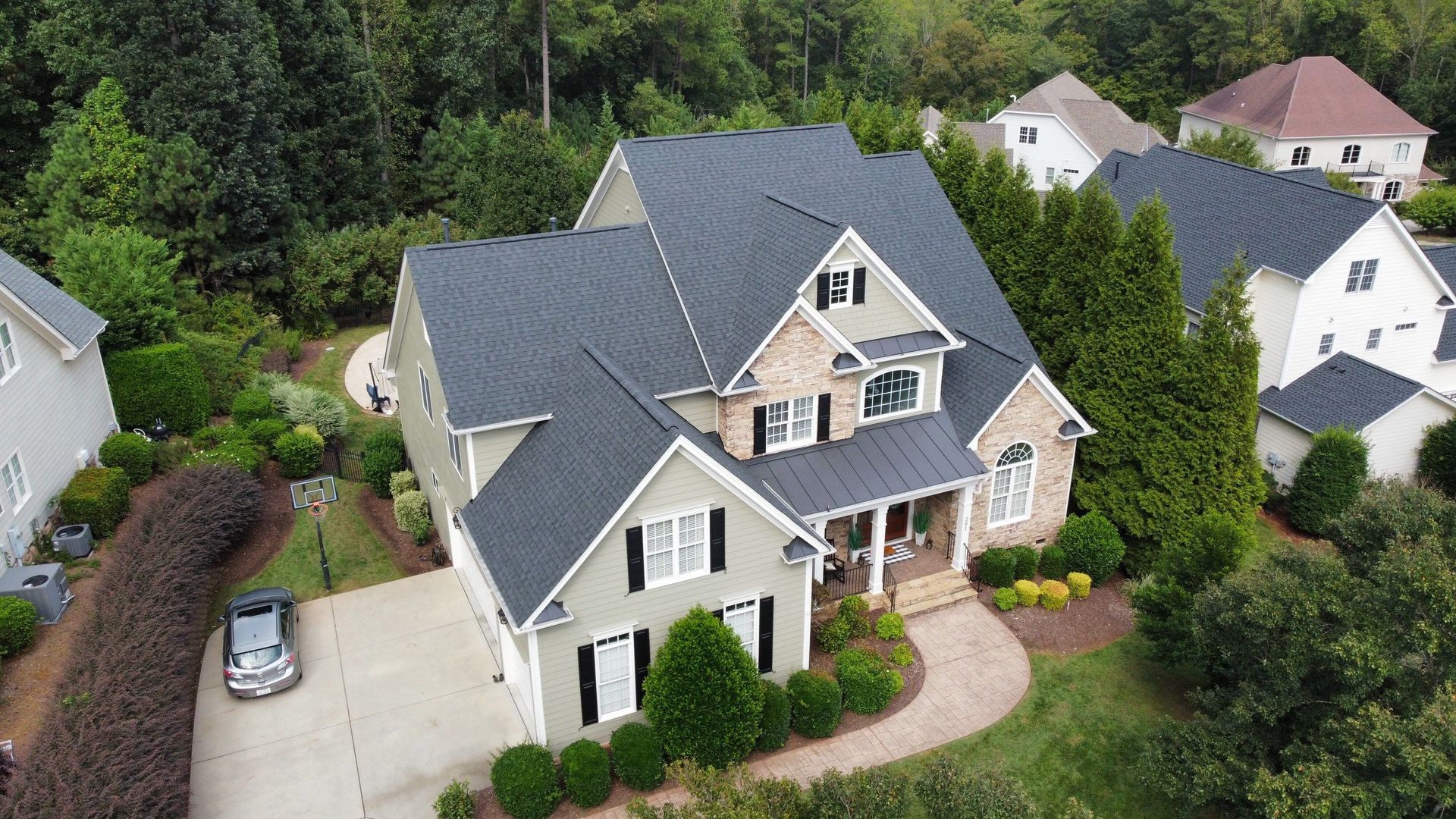 Aerial view of a two-story house with a gray roof, beige and green siding, and a circular driveway.
