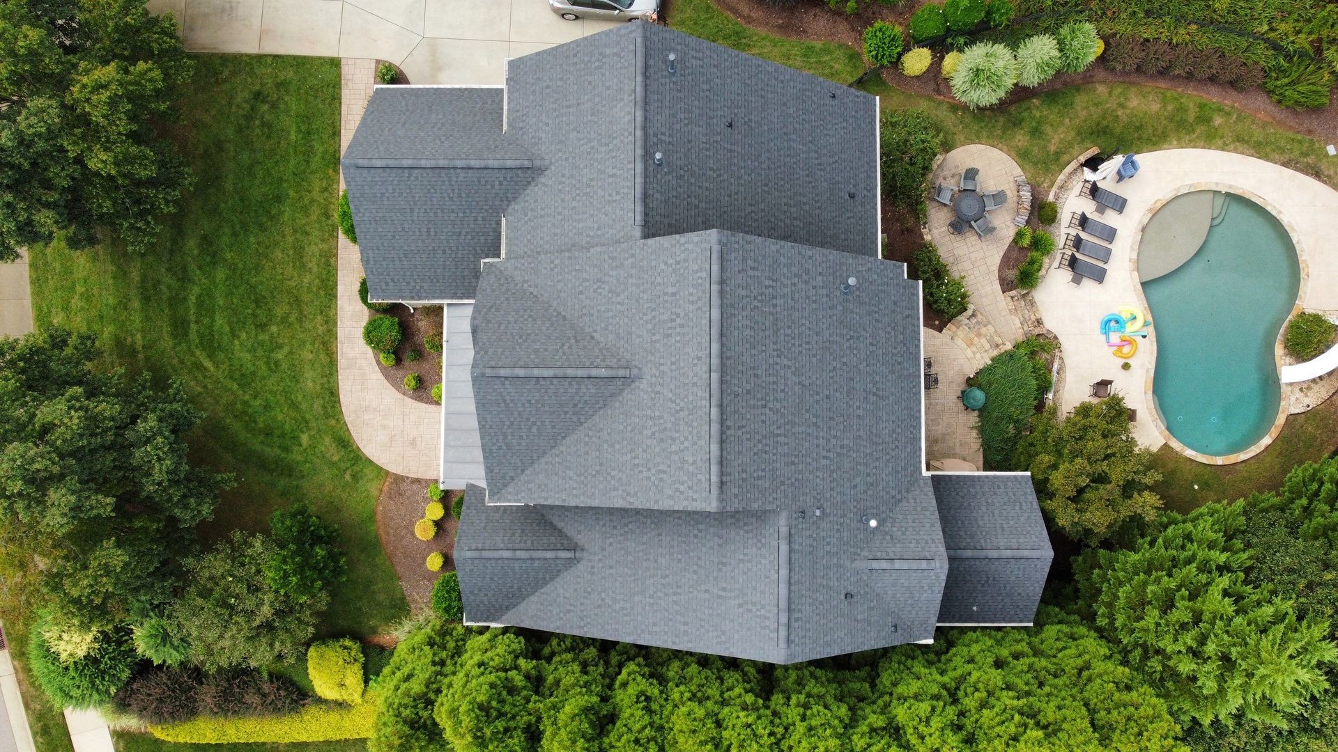 Overhead view of a house with a dark gray roof, next to a pool and lawn.