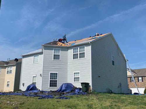 Roofers working on a residential house with light gray siding under a blue sky.