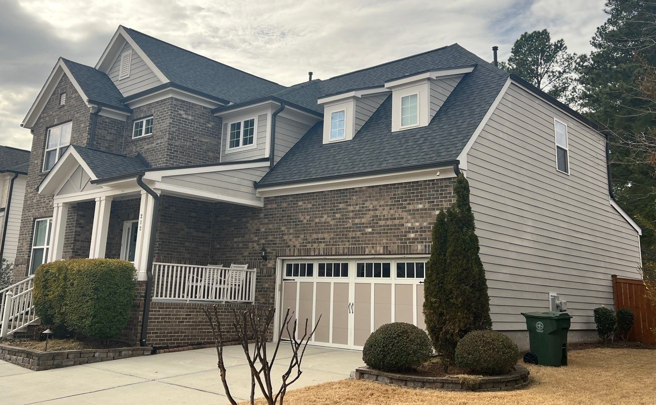 Exterior view of a house with a section of the roof and a window reflecting a cloudy sky.