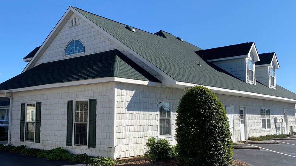 White building with dark green roof and shutters, under a clear blue sky.
