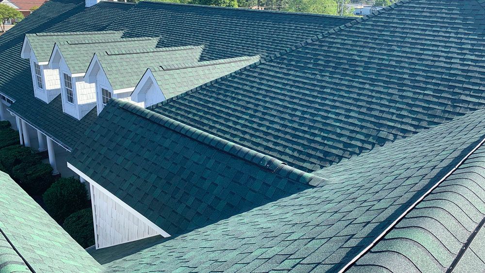 Green shingled roof with multiple gables on a white building, seen from above.