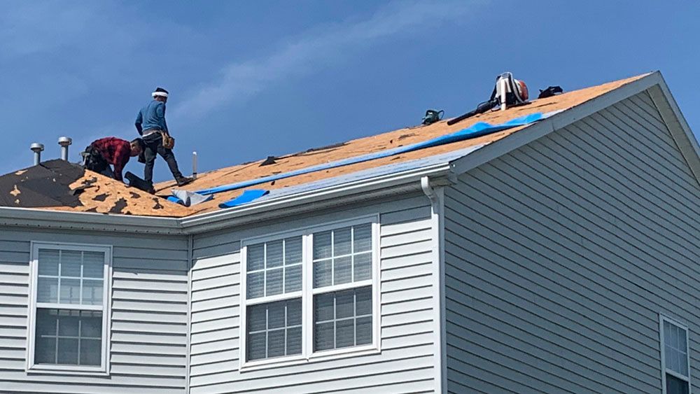 Roofers replacing a roof on a two-story house under a blue sky.