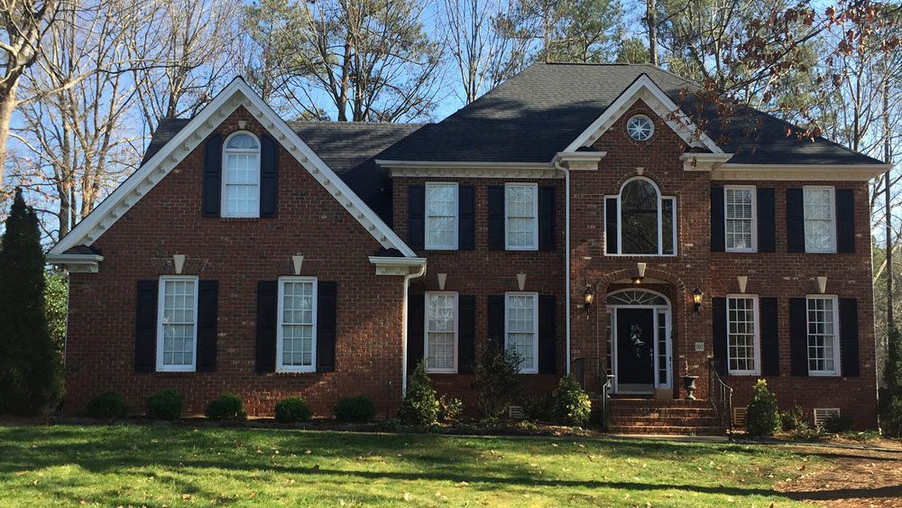 Red brick two-story house with black shutters and door, arched window, and lush green lawn.