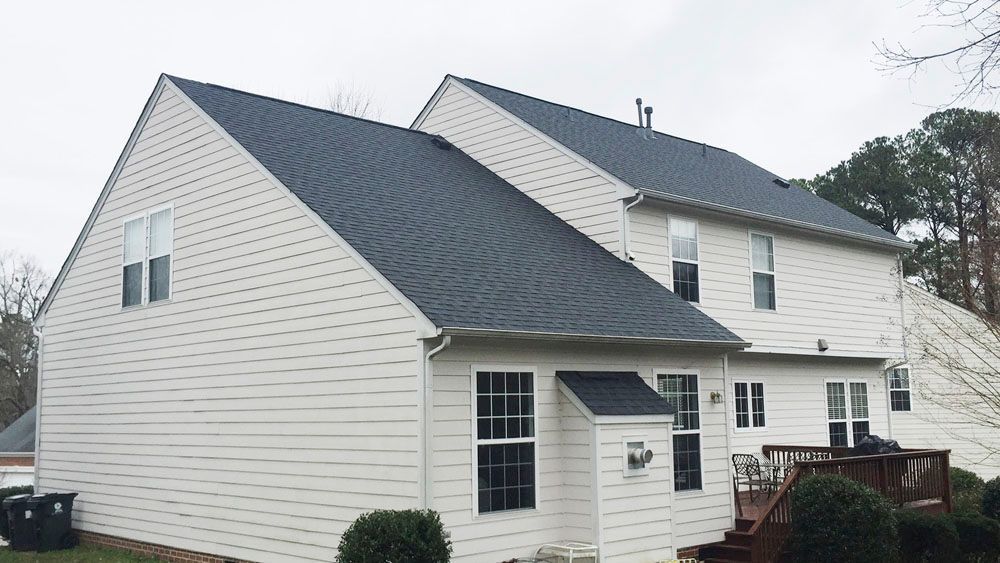 Two-story house with dark gray roof and cream-colored siding; backyard view with windows and a small deck.