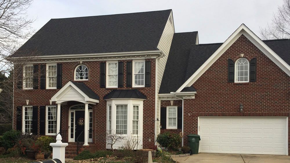 Two-story brick house with a black roof, white trim, and a two-car garage.