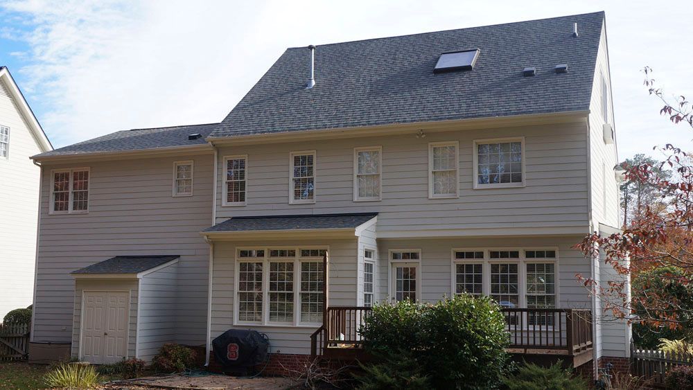 Back view of a two-story light gray house with a dark roof and a small wooden deck.