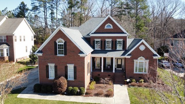 Brick house with black shutters, a covered porch, and a gray roof, in a residential neighborhood.