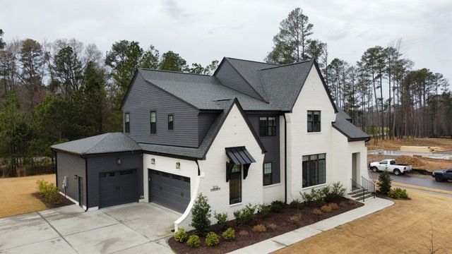 Modern two-story house with gray roof and accents, white facade, attached garage, and landscaped yard.