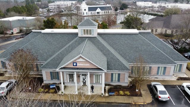 Bank building with white columns, blue accents, and a gray roof. Cars parked in front.