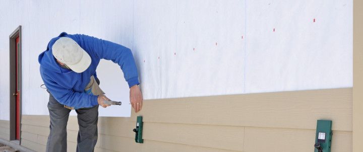Man installing siding on a building, using a hammer and level.