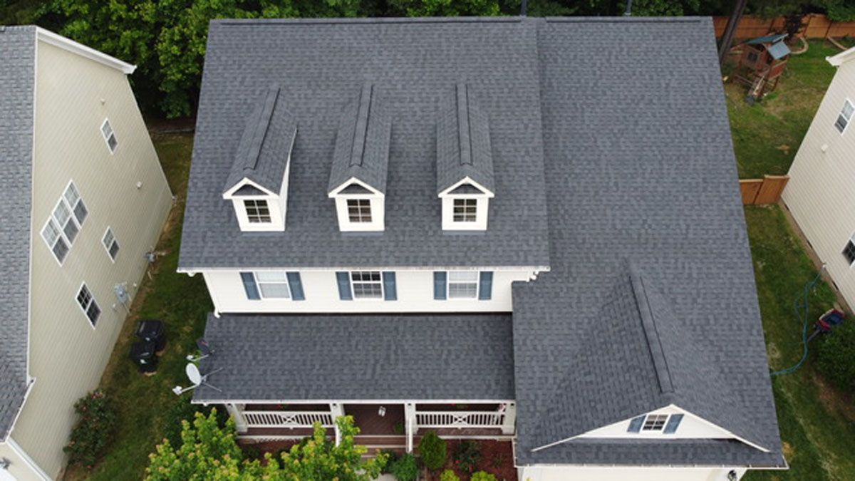 Gray asphalt shingle roof on a two-story house with dormers and neighboring houses.