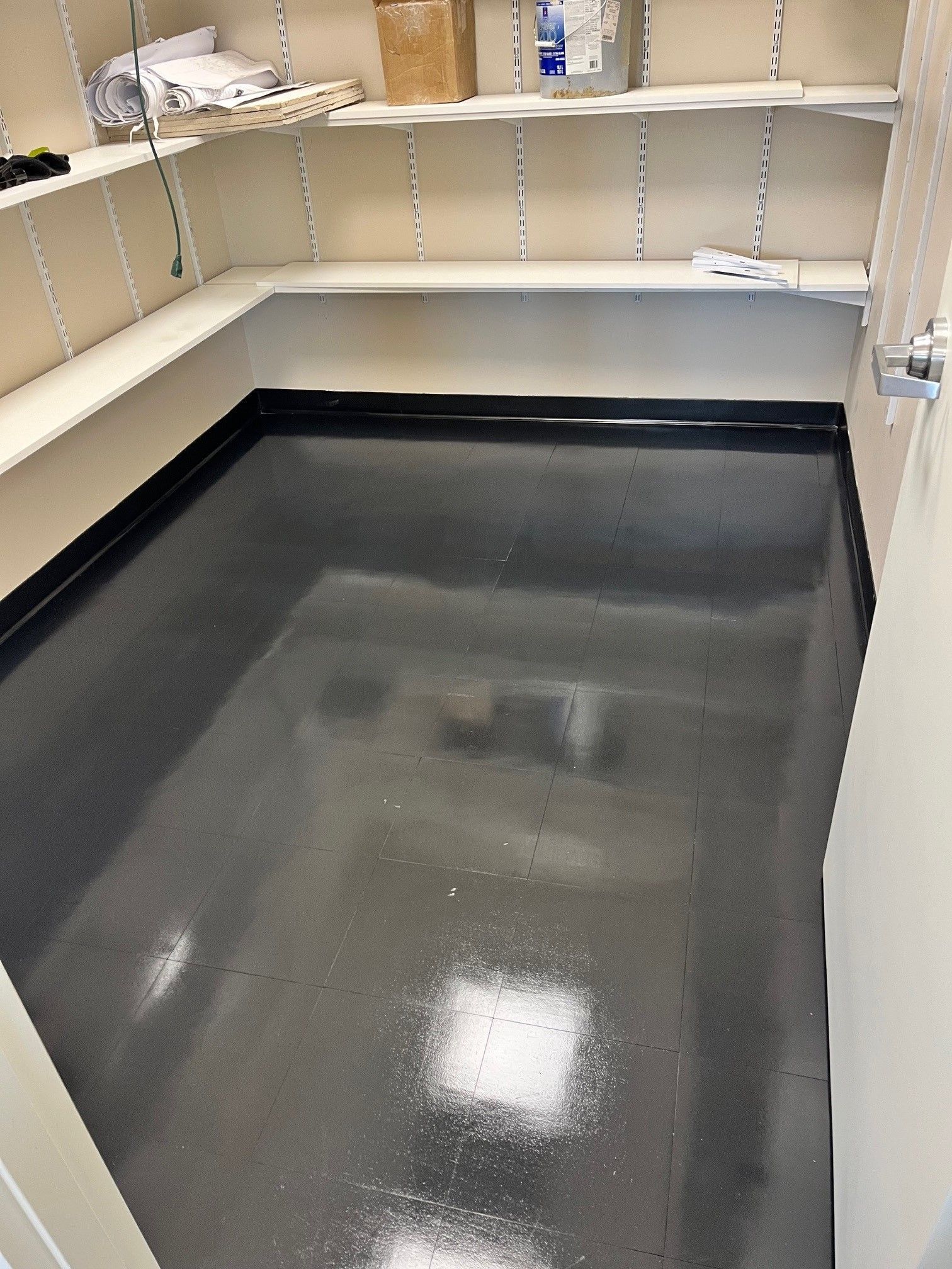 Empty room with dark gray floor, white shelves, and light tan walls.