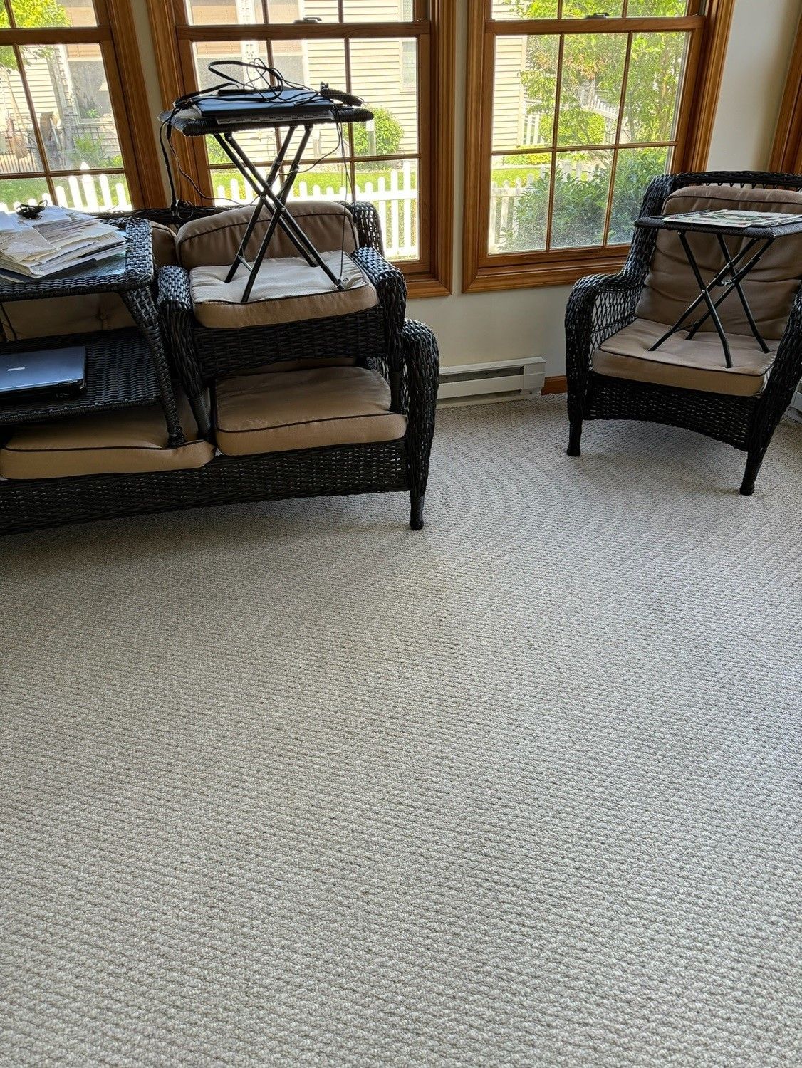 Wicker furniture with beige cushions in a room with beige carpet and large windows.