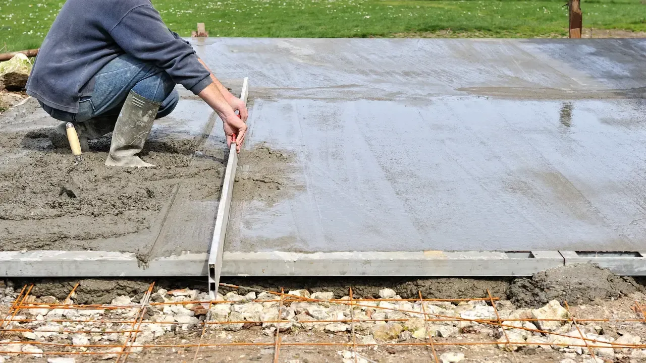 A person measuring and smoothing a concrete slab