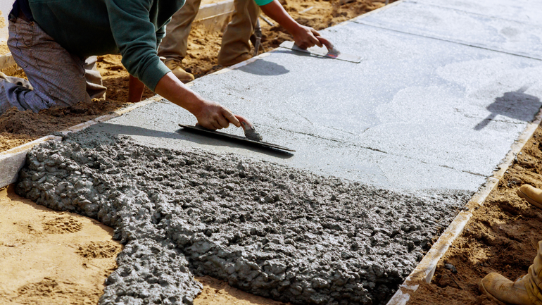 A person smoothing out a concrete sidewalk section with hand tools