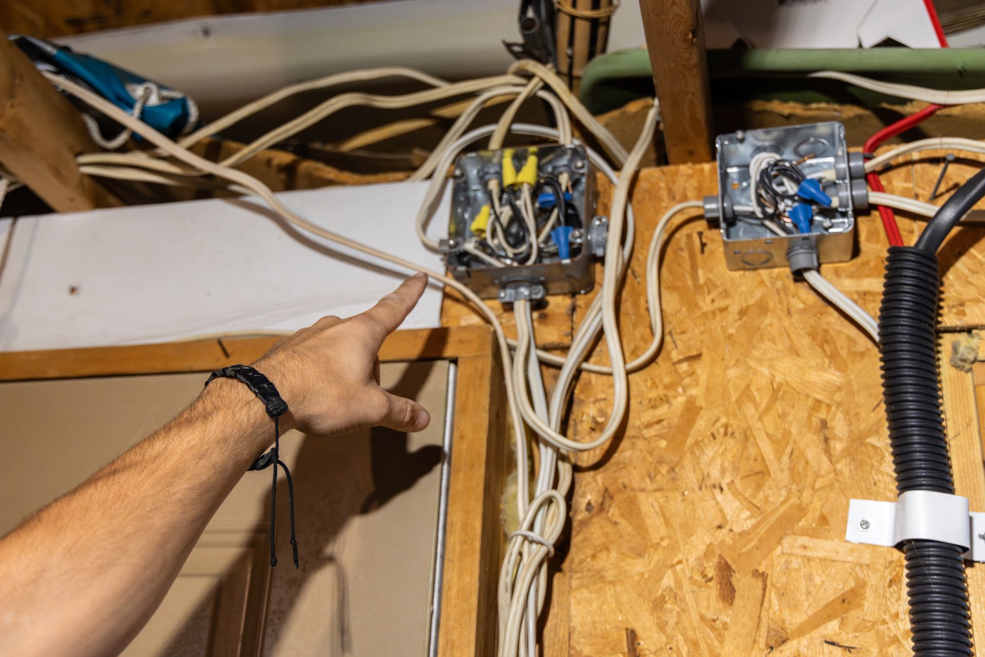 Hand pointing to tangled electrical wiring in a wooden-paneled room.