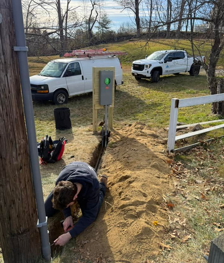 Two technicians in yellow shirts and hard hats inspect electrical wiring at a solar panel site.