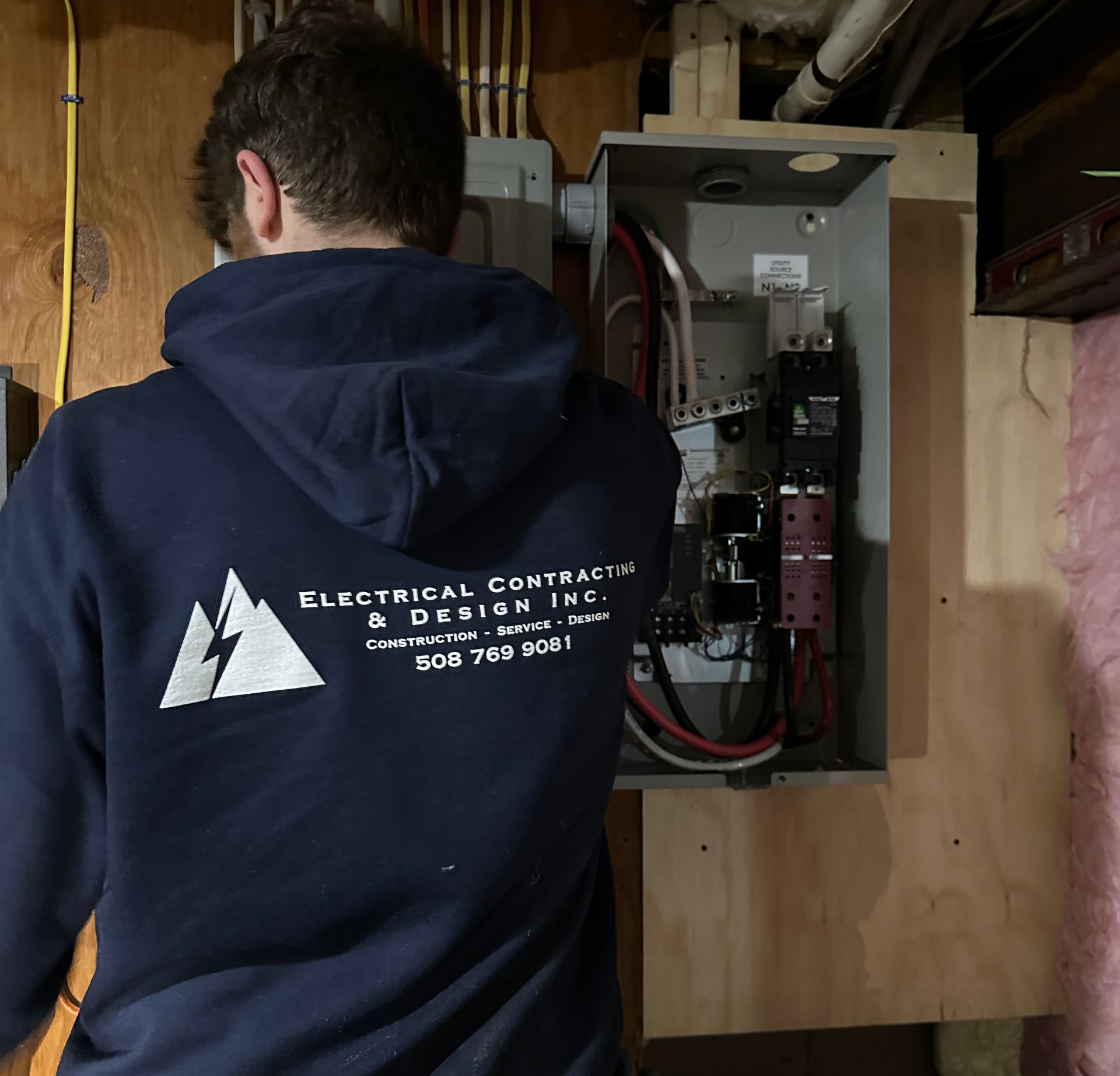 Hand testing an electrical outlet with red and black probes. Wires are visible, wall is white.
