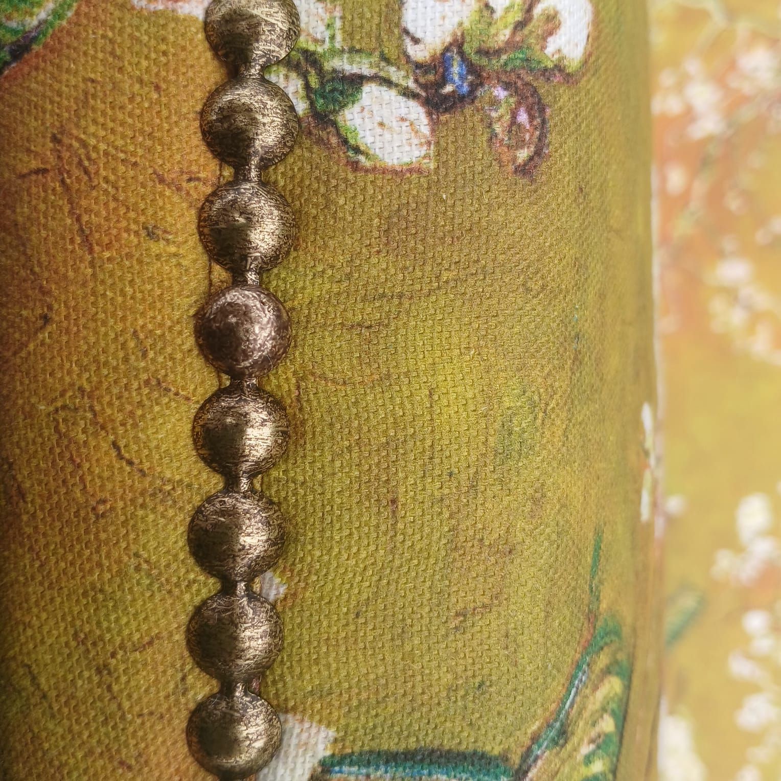 Chain of brown spheres against a textured olive green fabric with floral print.