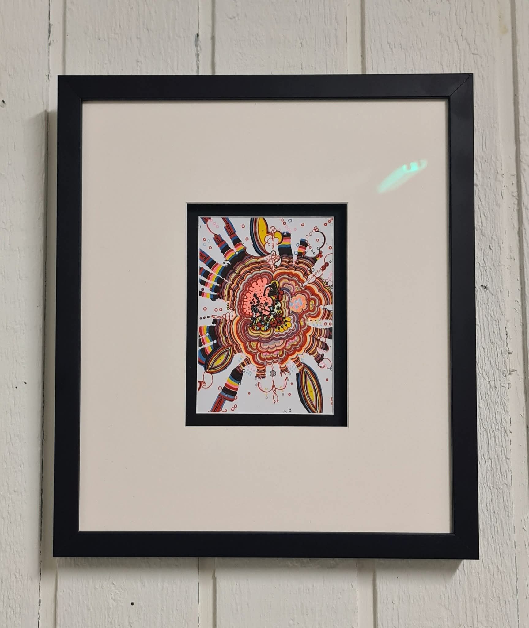 Ingelijst kunstwerk: abstracte, rood-oranje vormen met zwarte lijst, op een crèmekleurige passe-partout aan een witte muur.