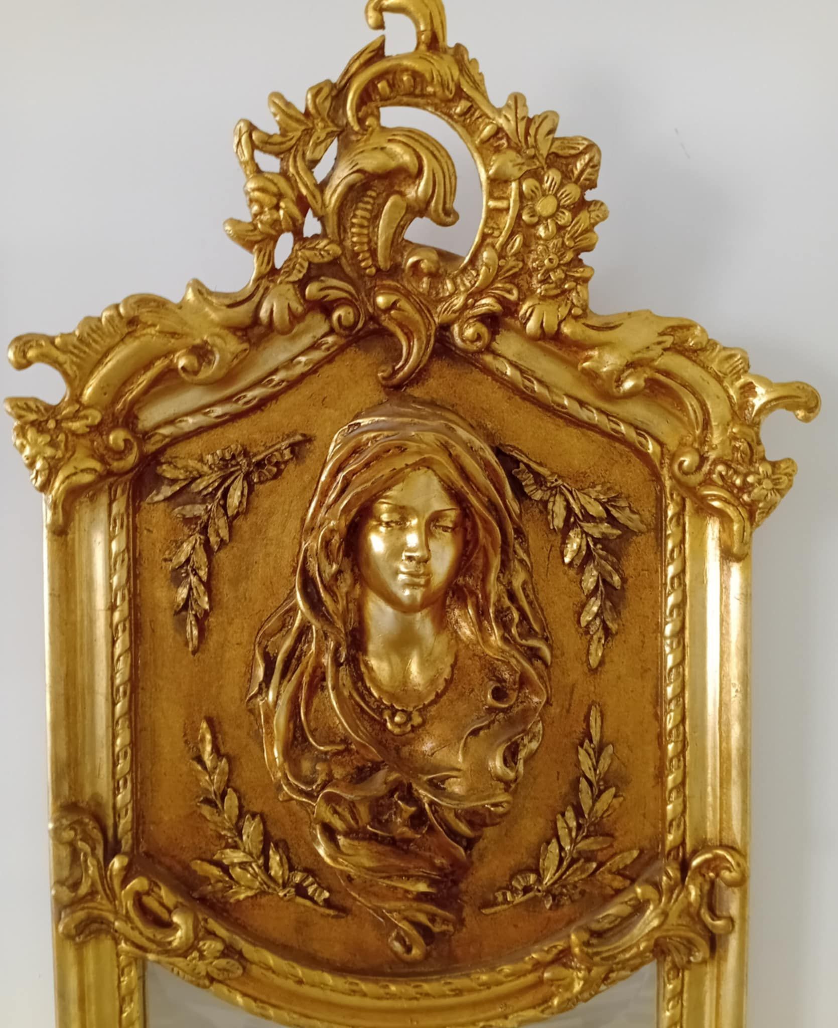 Een sierlijk reliëf van het gezicht en de borst van een vrouw, omlijst met goud, versierd met bloemendetails.