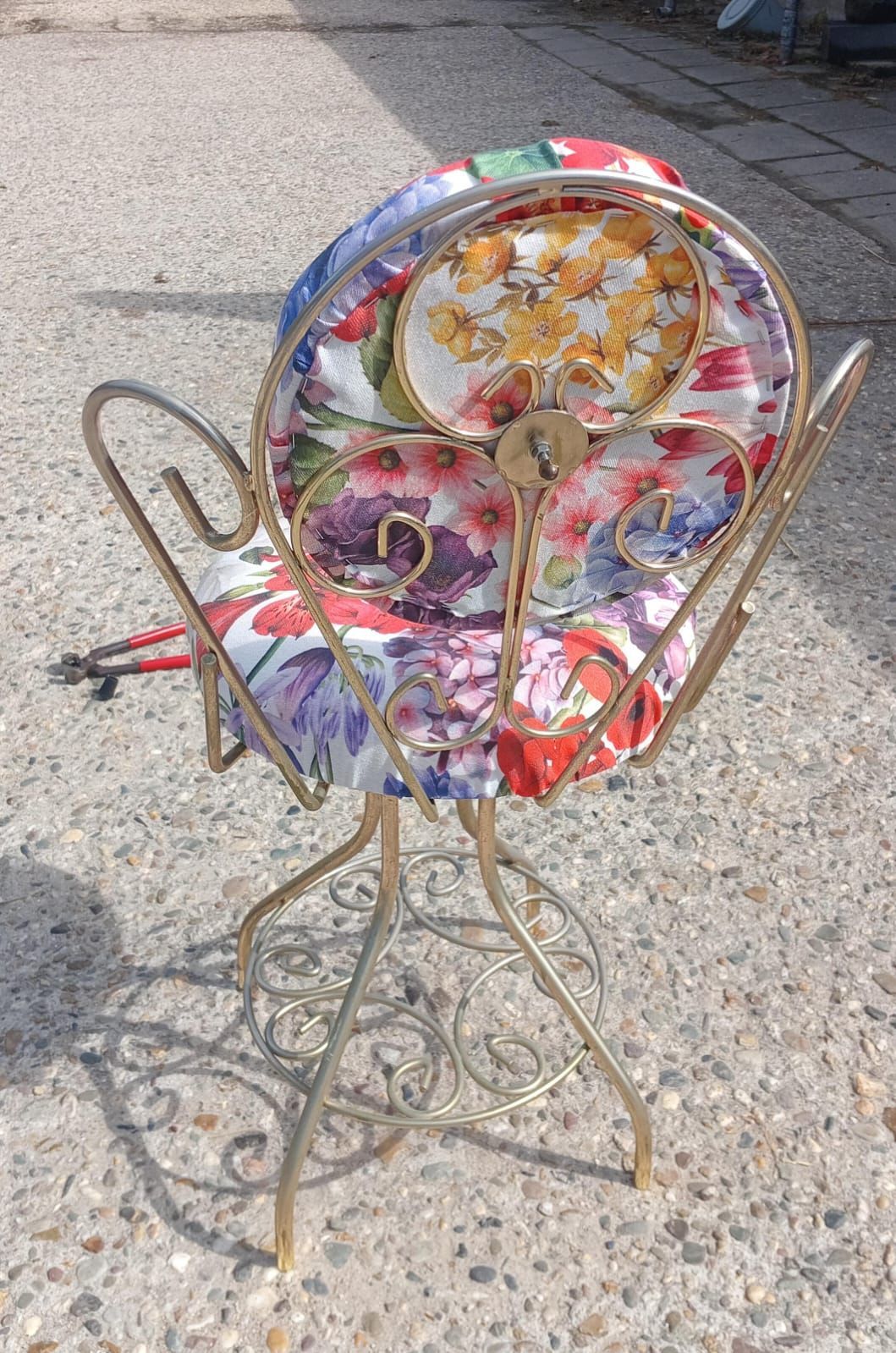 Gouden metalen stoel met kussens met bloemenmotief en borden, op beton.