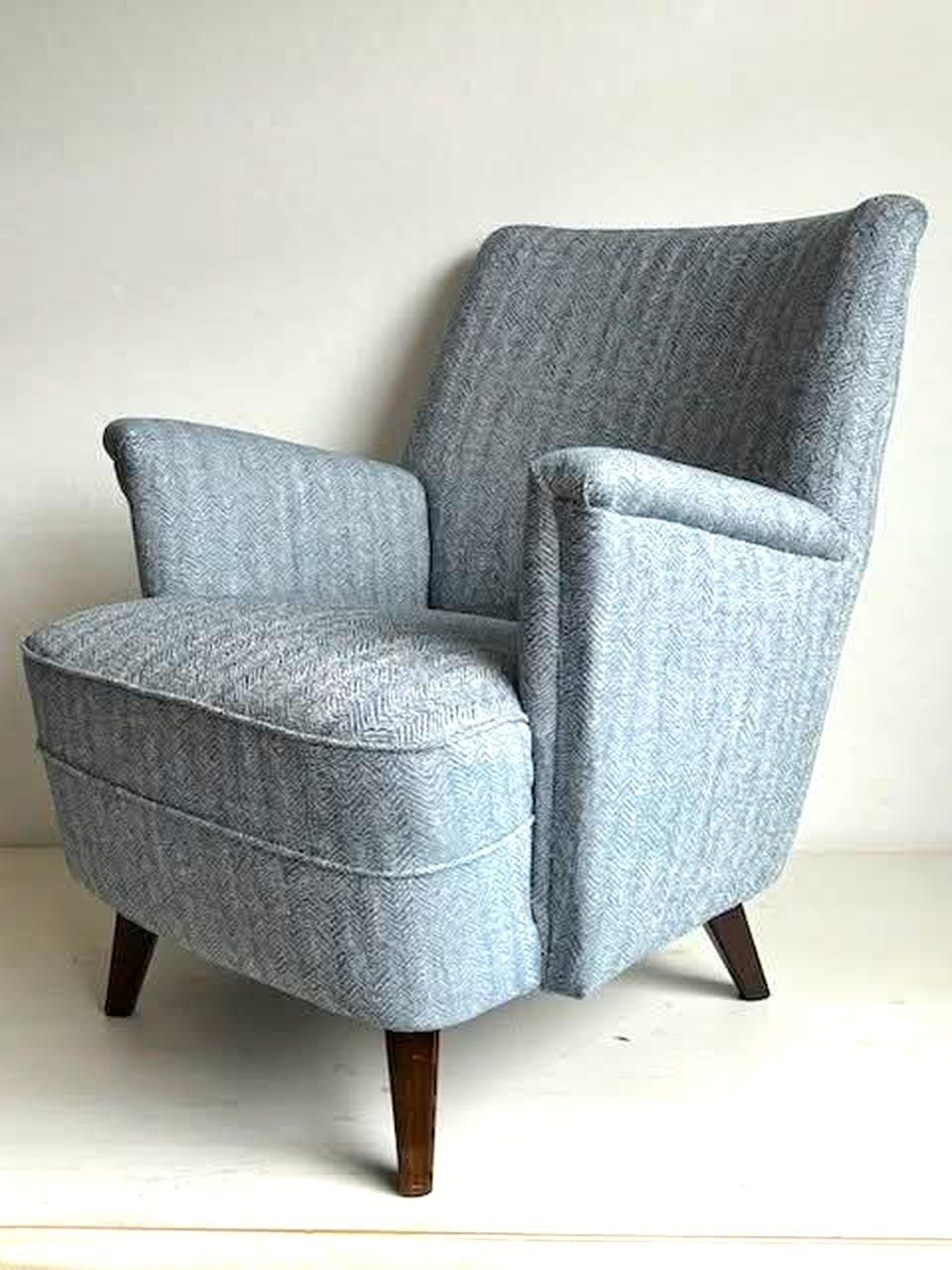 Blauwe gestoffeerde fauteuil met hoge rugleuning en houten poten.