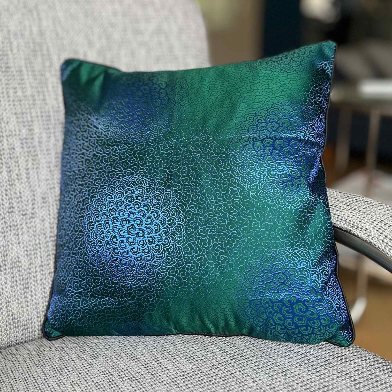 Smaragdgroen en blauw kussen op een grijze stoel.
