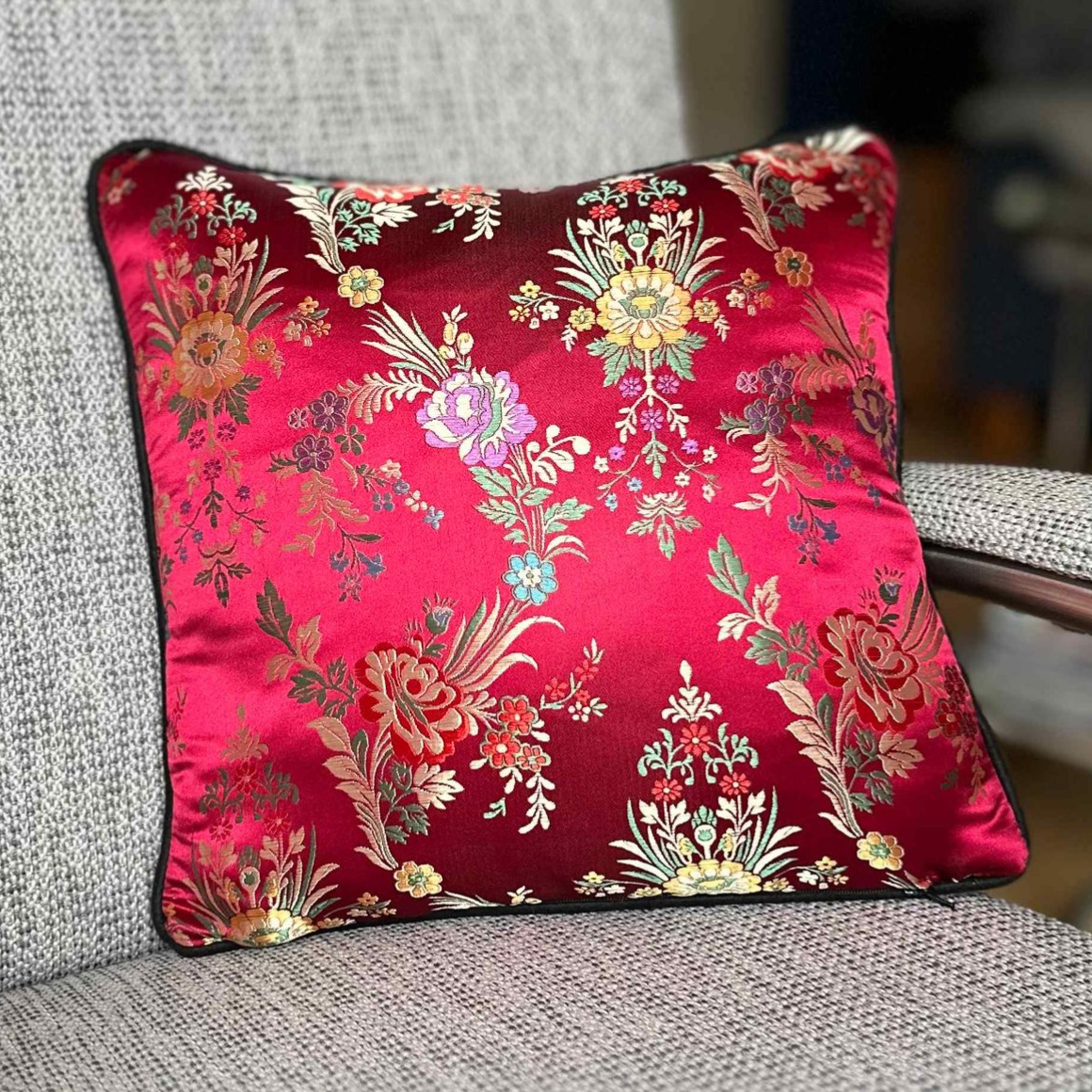 Rood bloemenkussen met zwarte biezen op een grijze stoel.