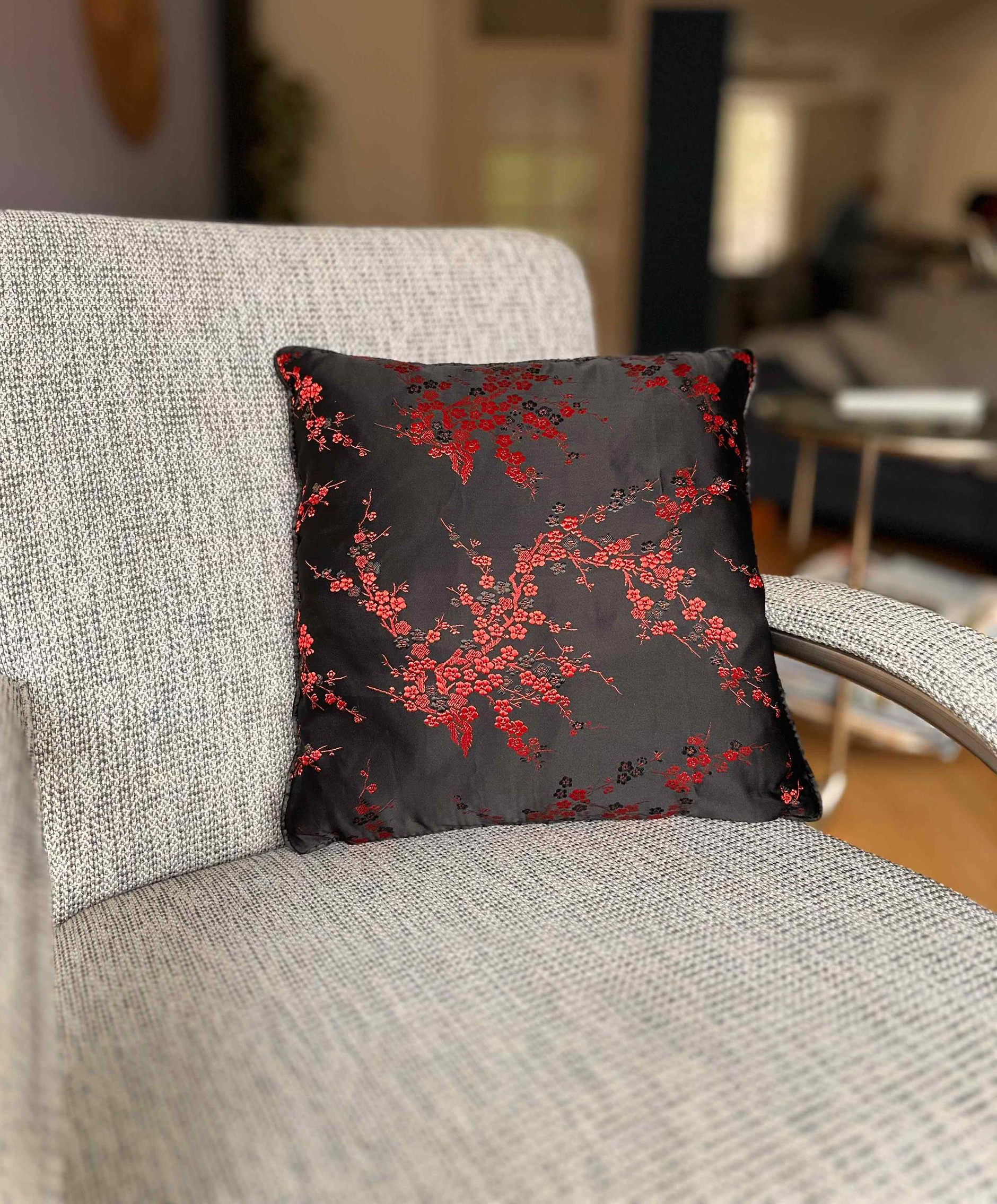 Zwart kussen met rood bloemenmotief op een grijze stoel, binnenshuis.