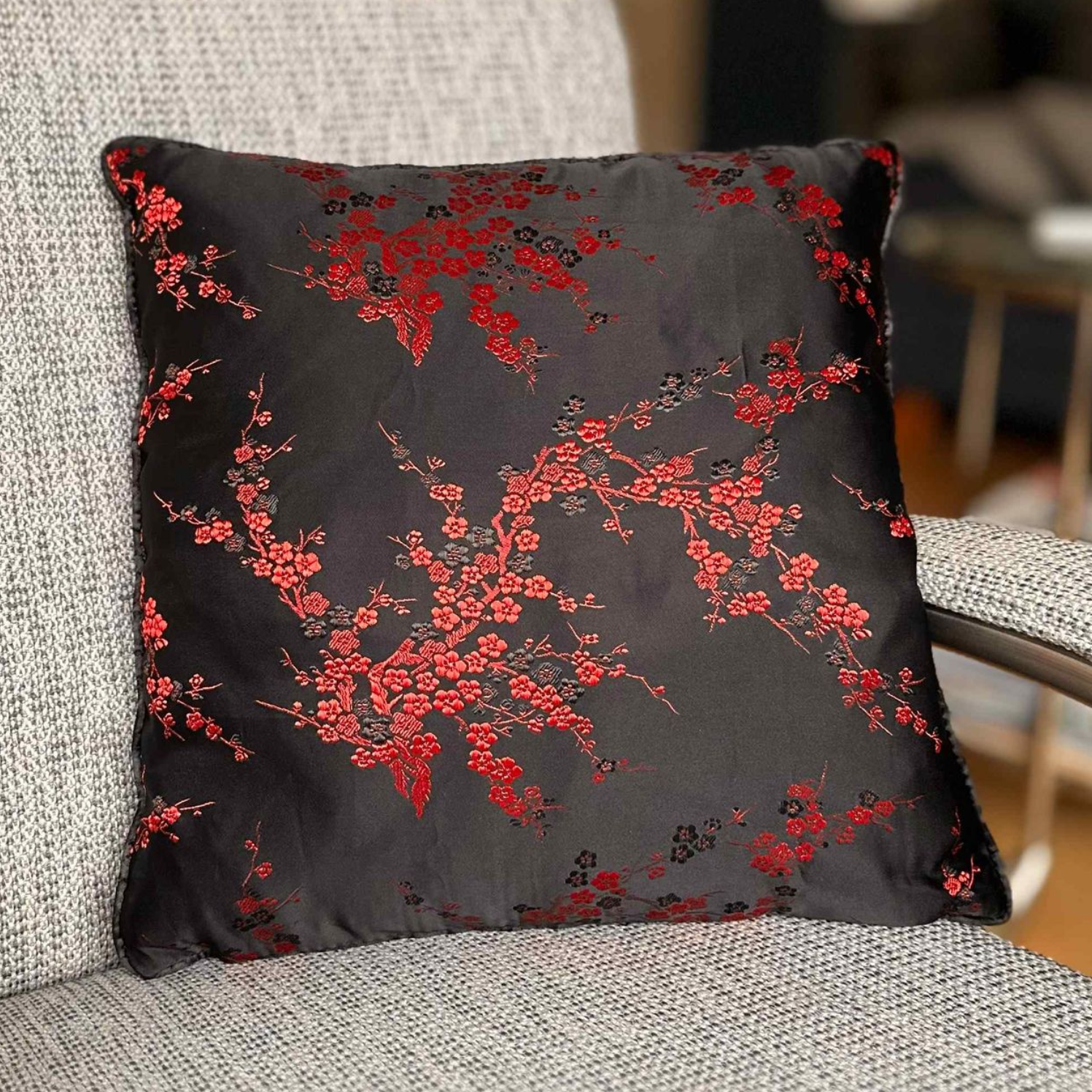 Vierkant zwart kussen met rood bloemenpatroon op een grijze stoel.
