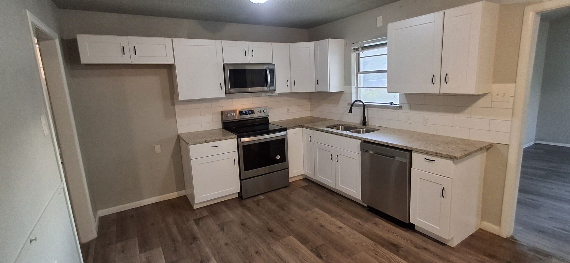 A modern kitchen with white cabinets, stainless steel appliances, and wooden floors.