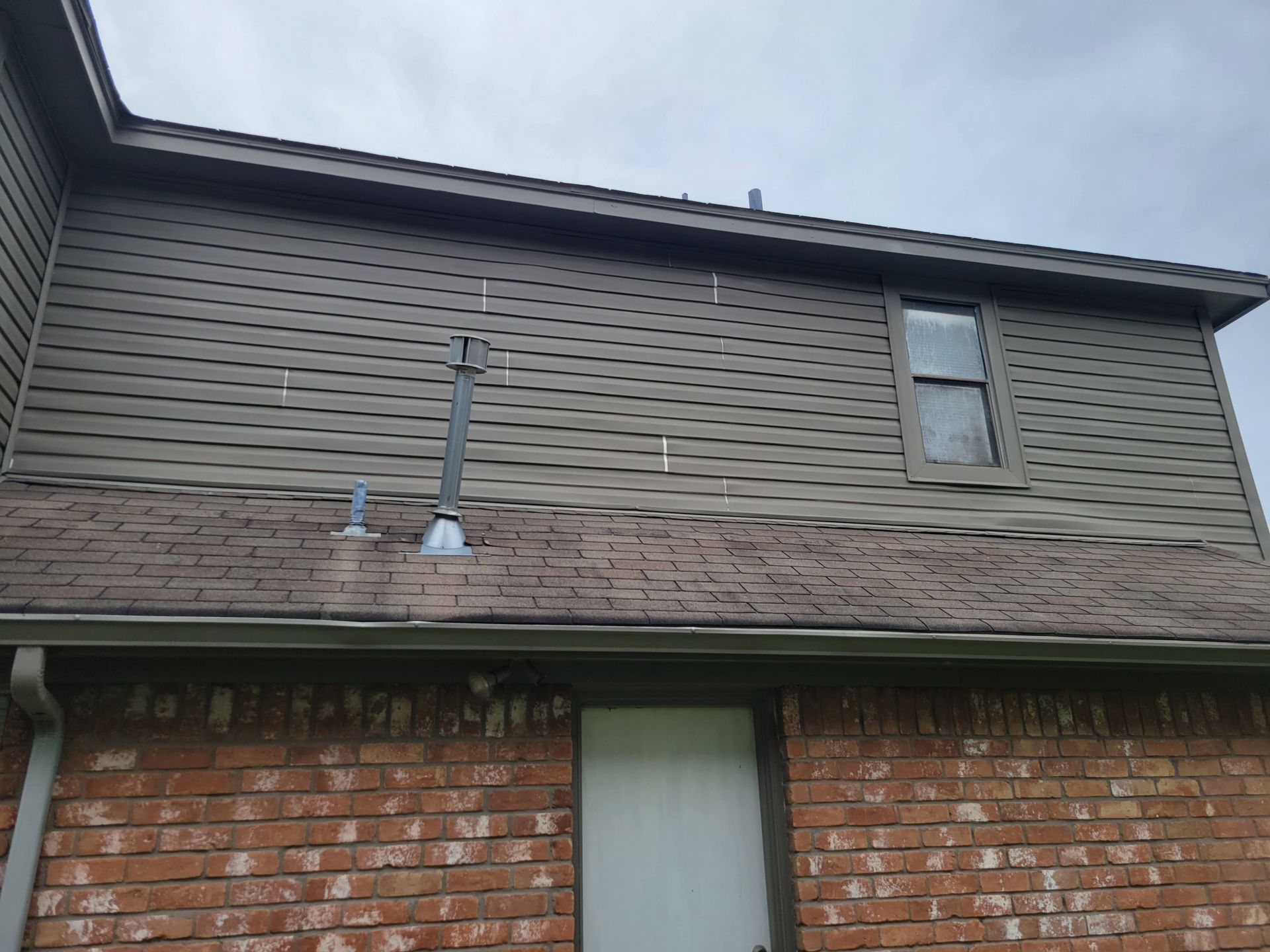 Exterior view of a house with brown siding, roof, and brick. Chimney extends from the roof.