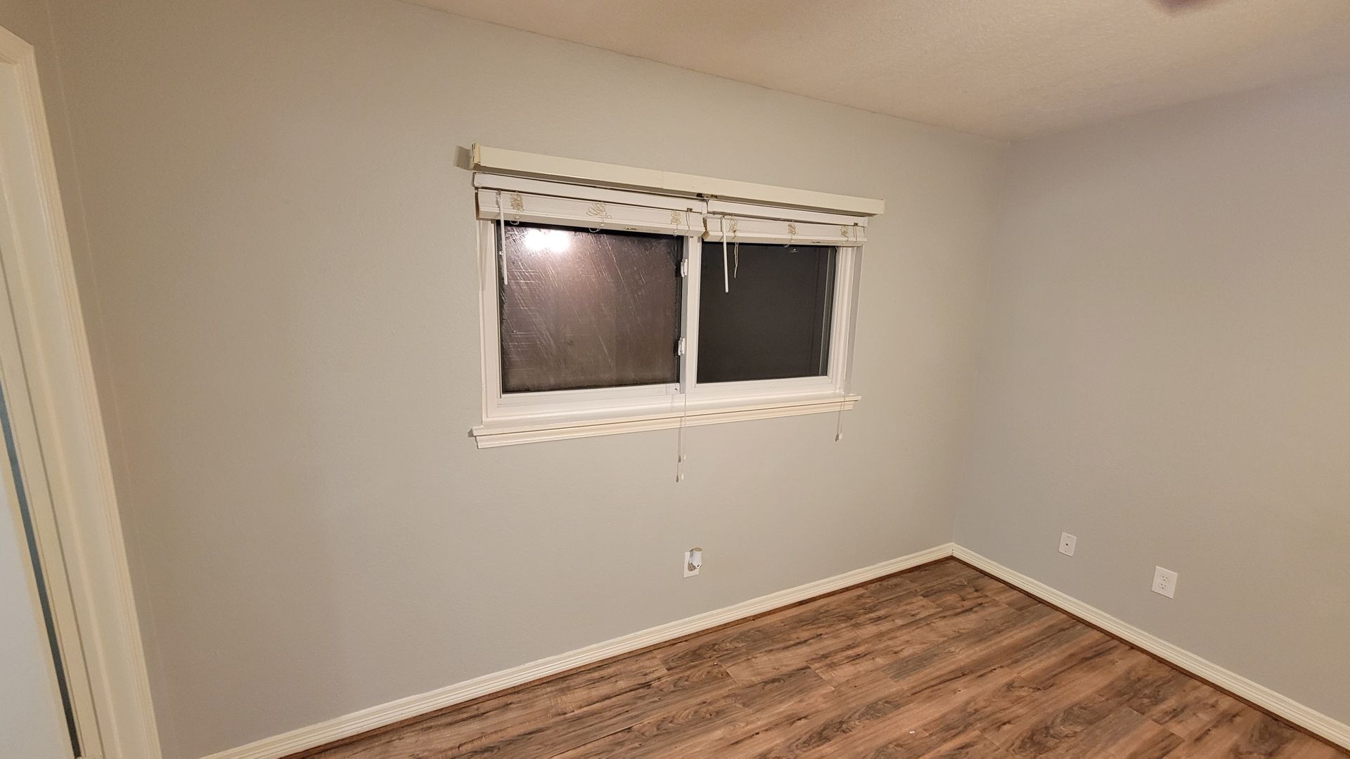 Empty room with a window, painted gray walls, and wood-look flooring. White blinds.