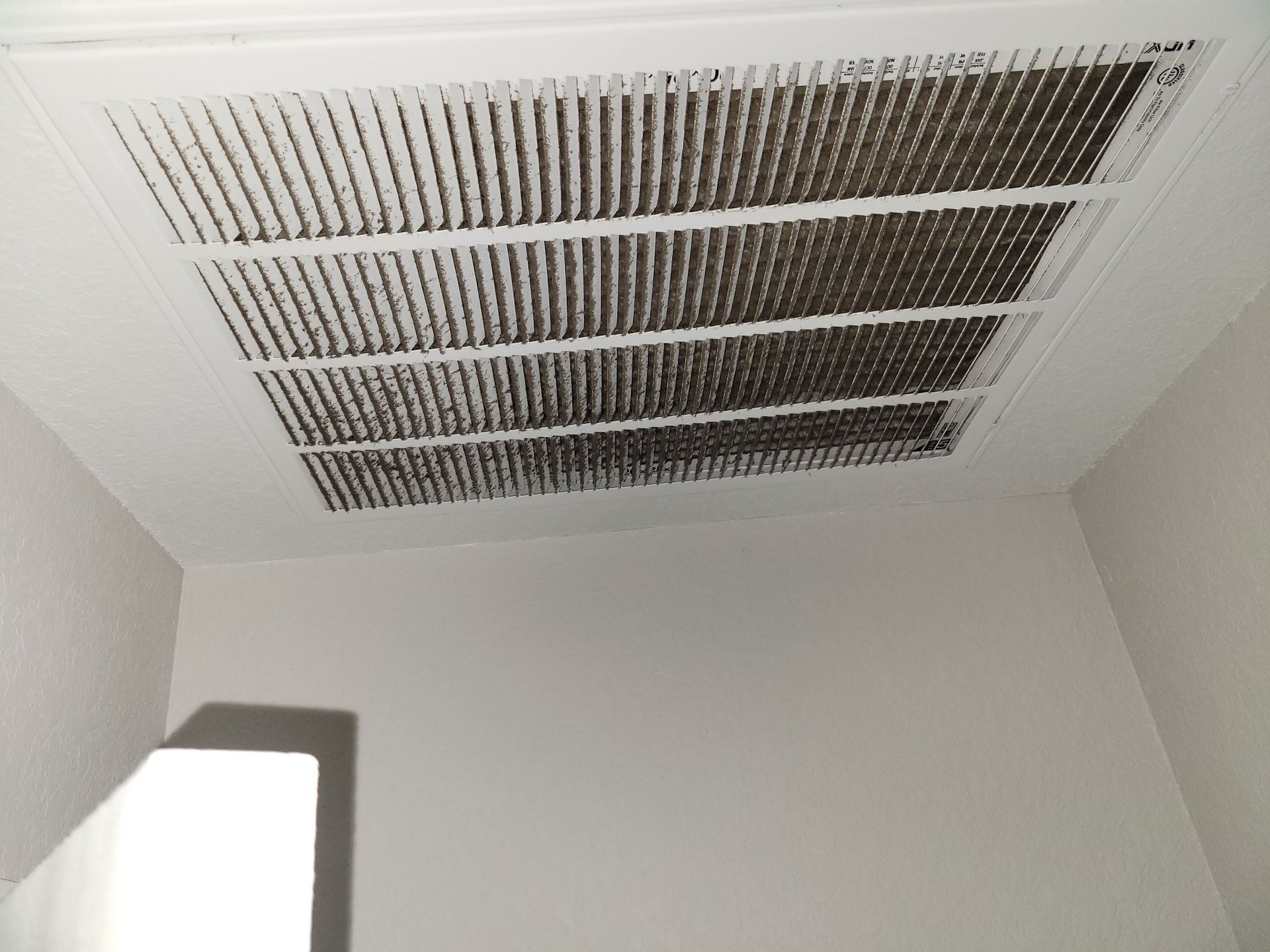 White ceiling air vent covered in dark dust.