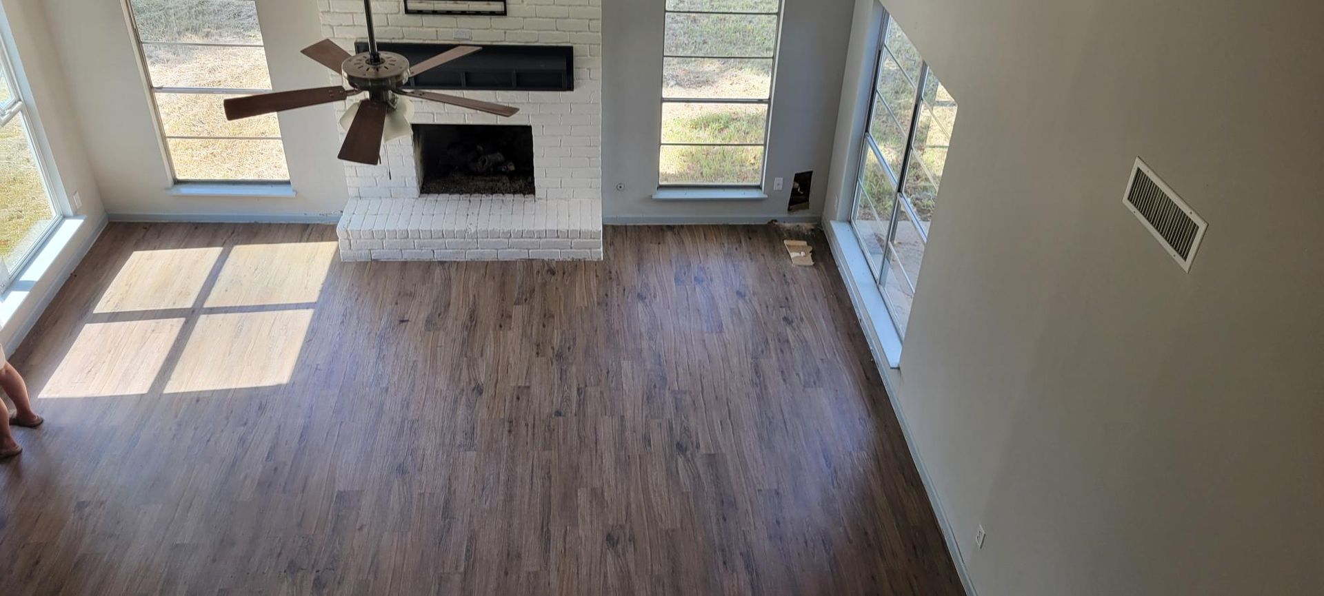 High-angle view of a living room with wood flooring, fireplace, windows, and ceiling fan.