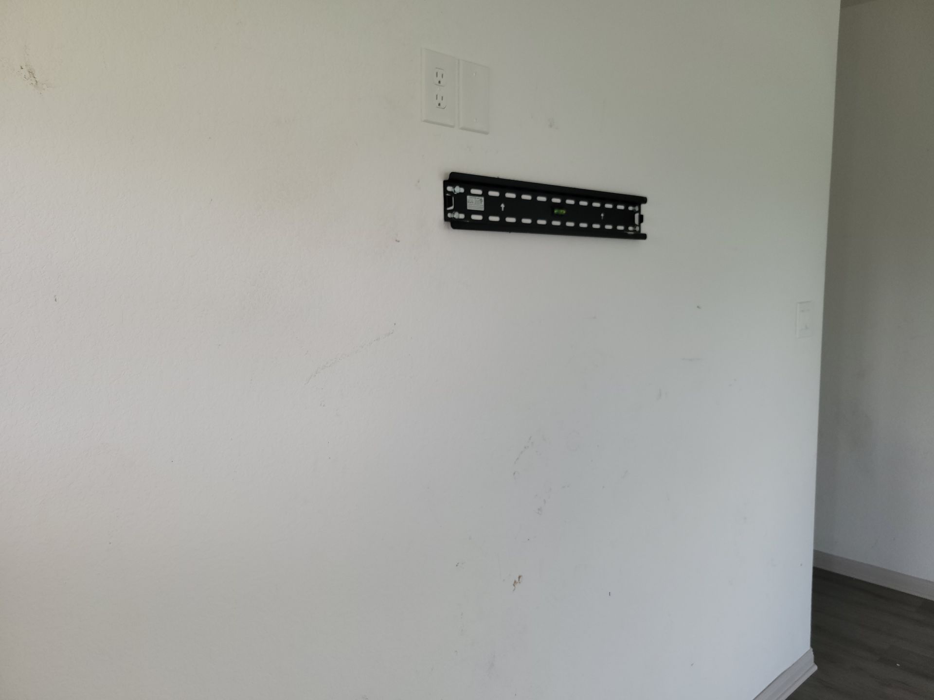 White wall with a mounted TV bracket and an electrical outlet.