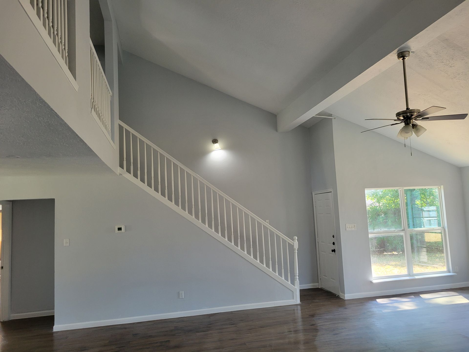 Interior view of a house with a staircase, high ceilings, and a large window. The walls are light blue.