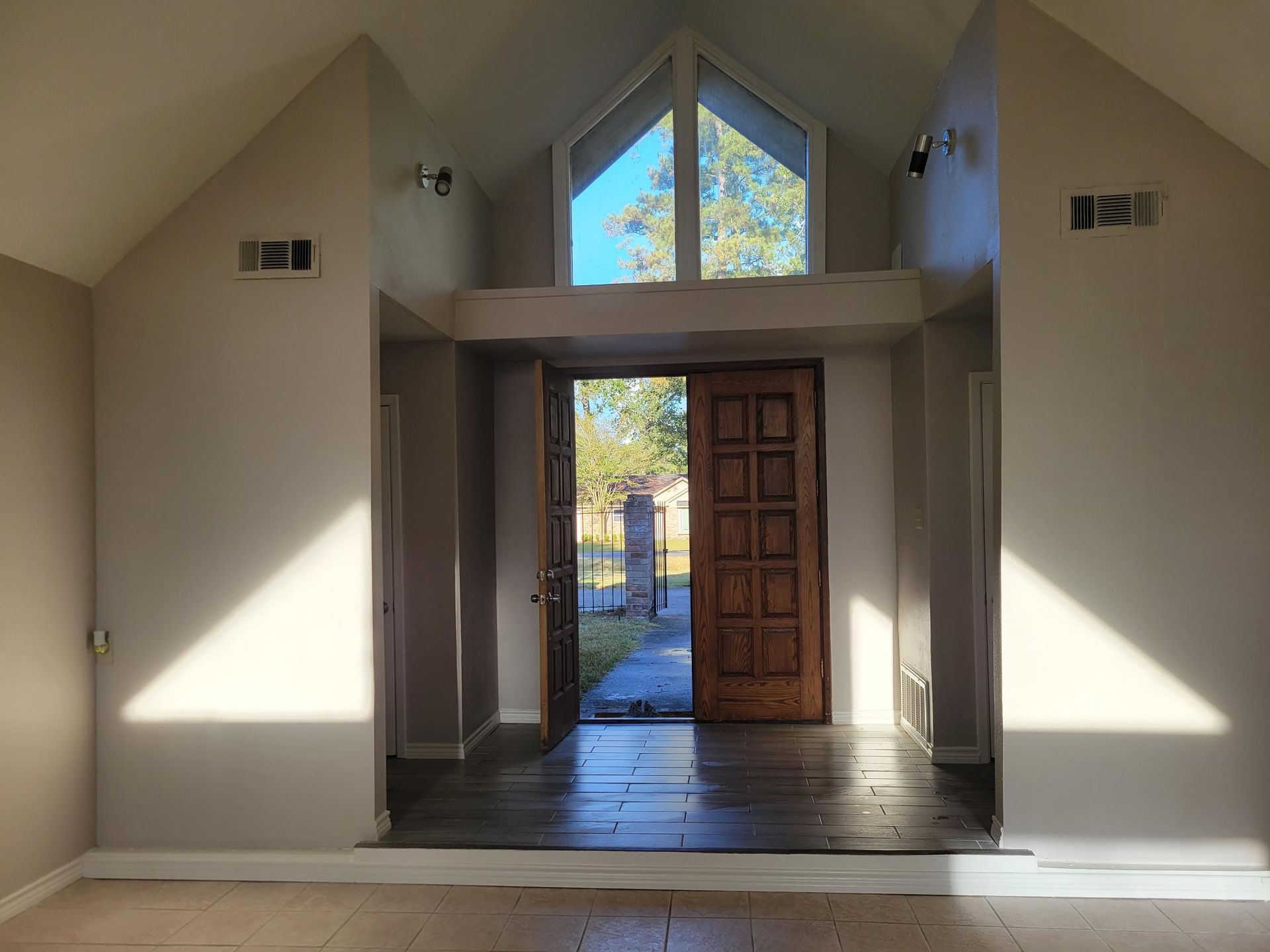 Interior view of a home's entryway with open wooden doors, sunlight, and a triangular window.
