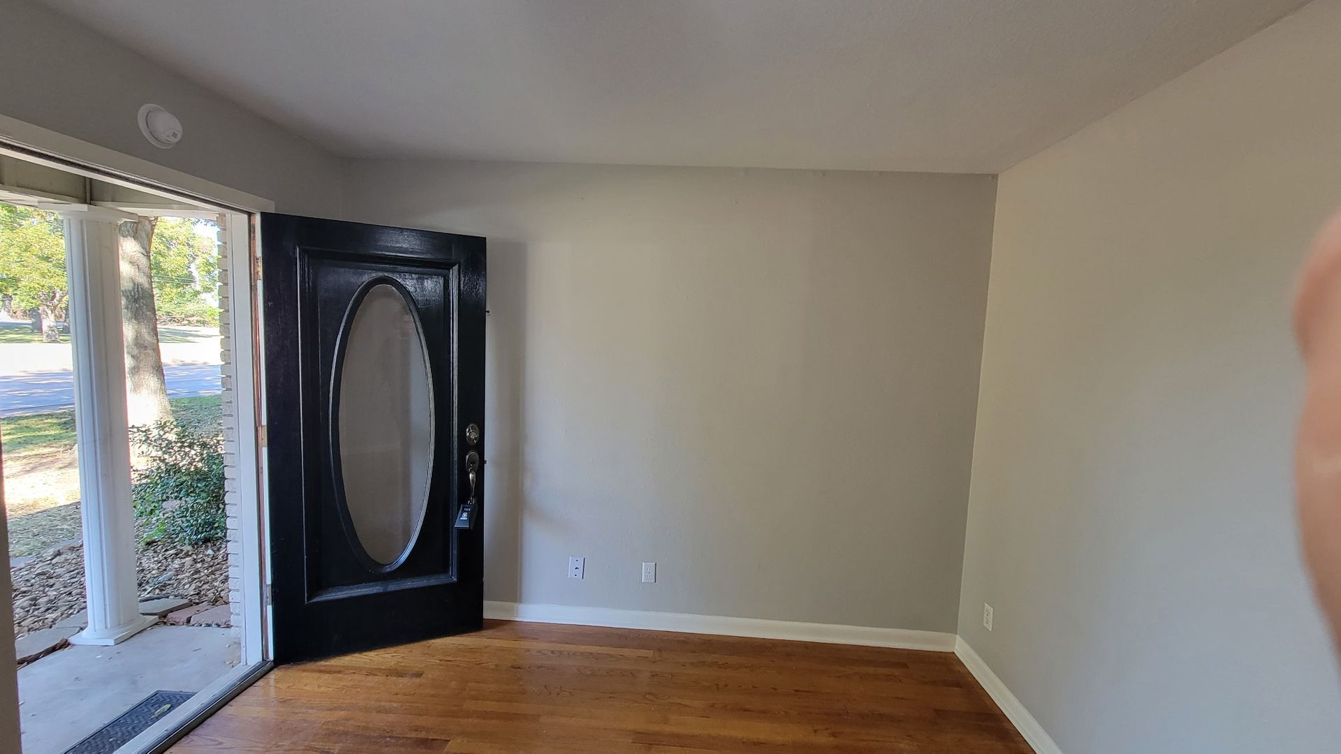 An interior room with hardwood floors, a gray wall, and a black front door with an oval window.
