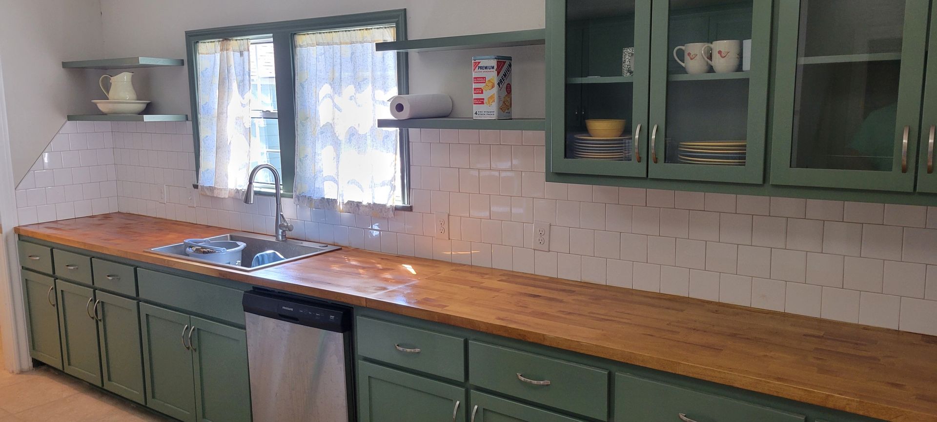 Kitchen with green cabinets, butcher block countertops, and white tile backsplash.